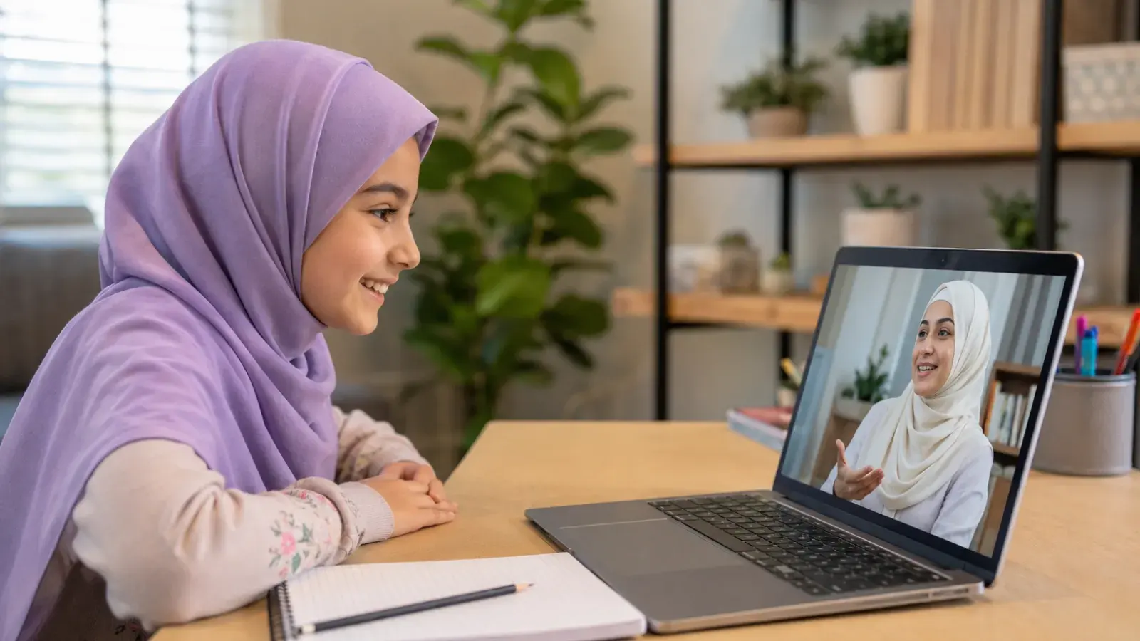 A girl smiling at her teacher during a live online Quran class on a laptop